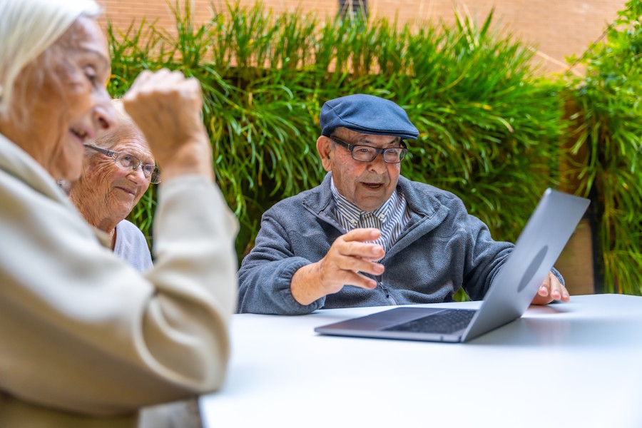 Group of older adults sitting at an outdoor table looking at a laptop together