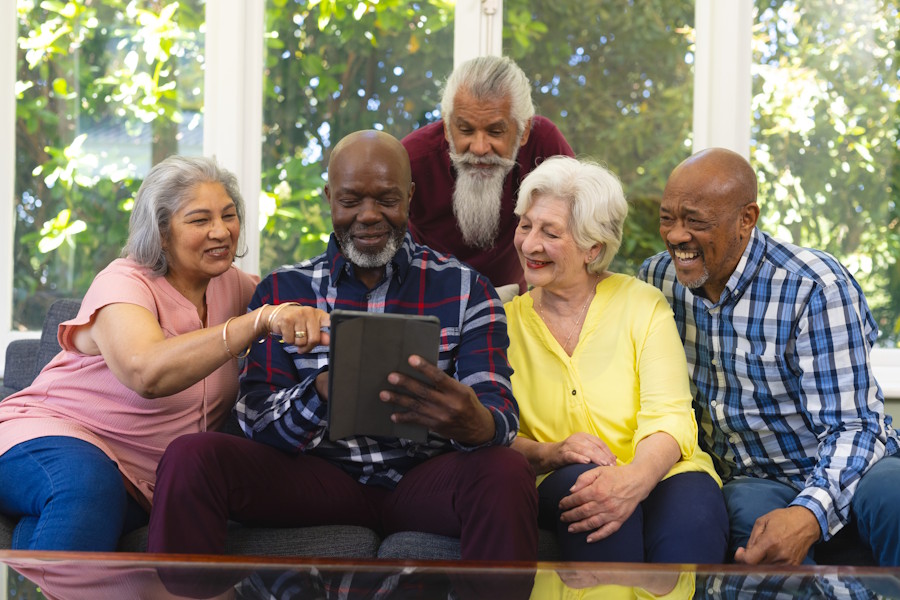 Diverse group of seniors sitting on a sofa smiling and looking at a tablet together