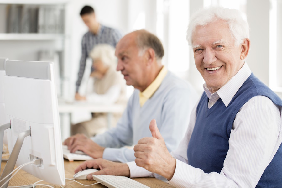 Smiling older man at a computer giving a thumbs up in a class