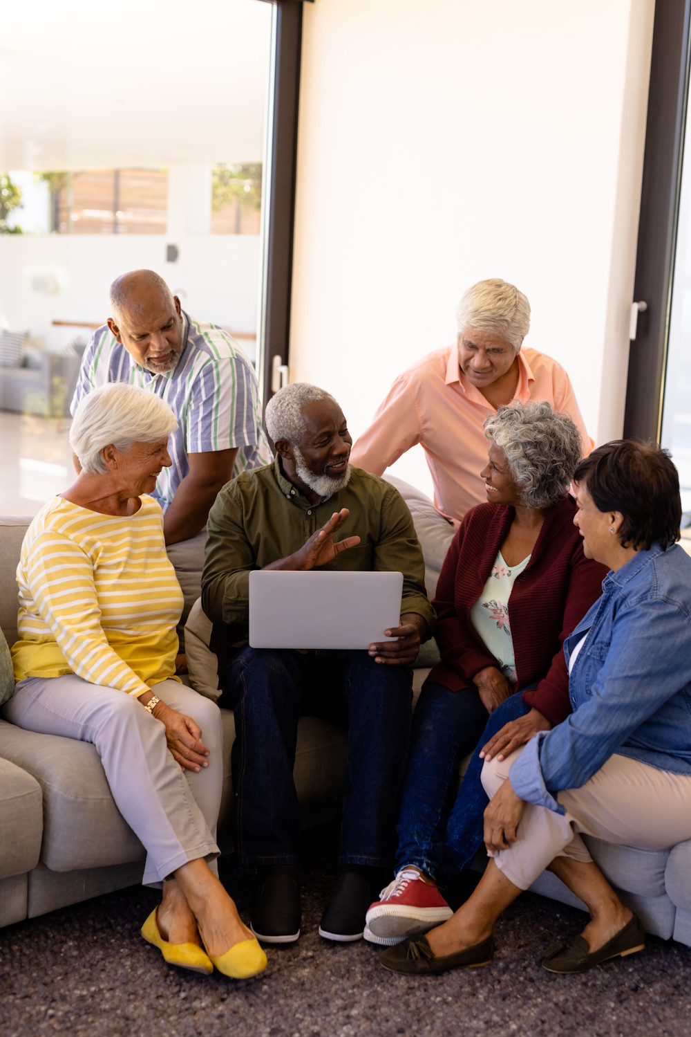 Multiracial group of seniors gathered around a laptop, talking and smiling