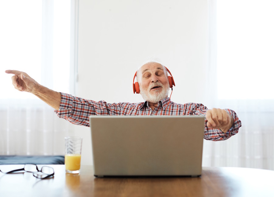 Older man wearing headphones smiling and moving to music while using a laptop