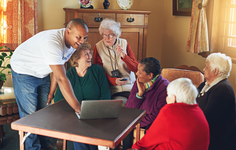 Volunteer helping a small group of senior women use a laptop together