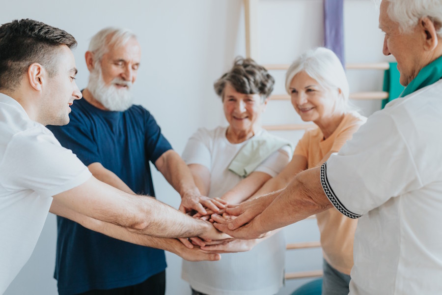 Instructor and seniors smiling in a circle with hands together to start a class