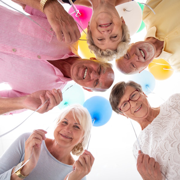 "Group of smiling seniors holding colorful balloons and leaning in a circle